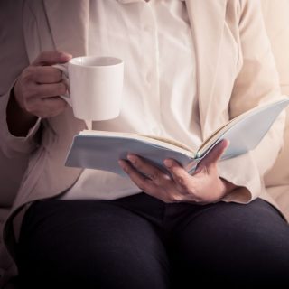 放松在沙发和阅读书的妇女，当拿着杯子时